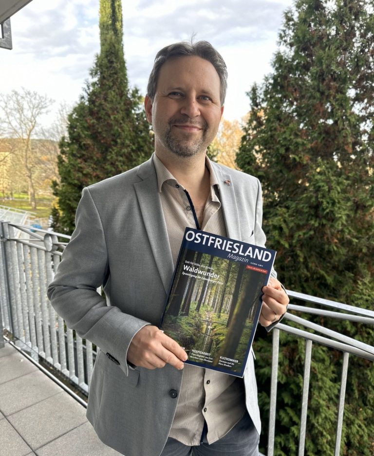 Eike F. Wilts in grauem Anzug hält eine Zeitschrift mit dem Titel „Ostfriesland“ in der Hand.