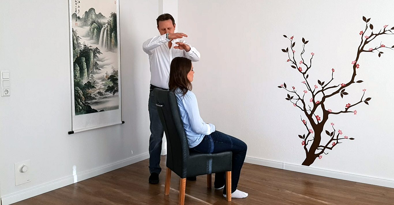 Ein Mann steht hinter einer sitzenden Frau und führt eine Behandlung aus.
