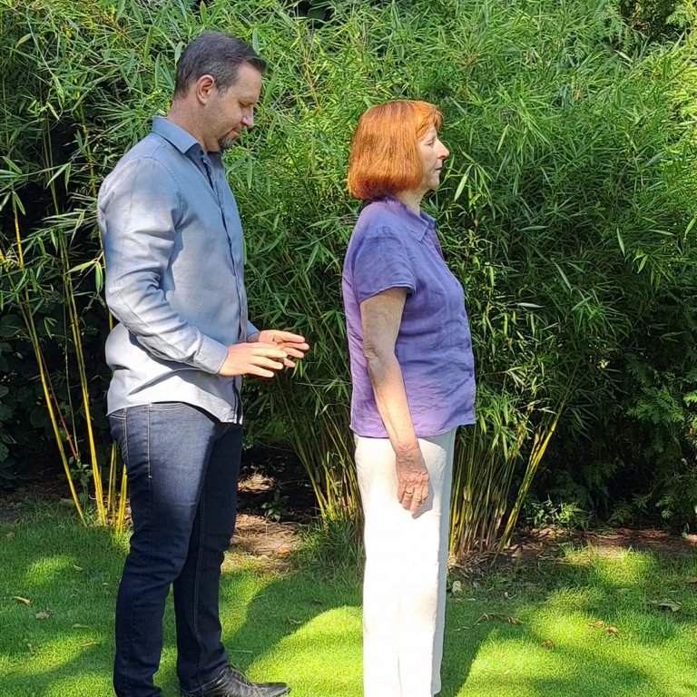 Mann steht hinter Frau im Garten, umgeben von hohen Pflanzen.
