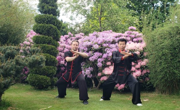Zwei Personen in schwarzer Kleidung üben in einem blühenden Garten.